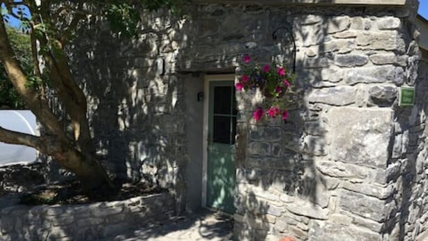 A stone building with a door and a hanging flower basket. - Cozy Irish cottage, located on the Wild Atlantic Way! (Fanore)