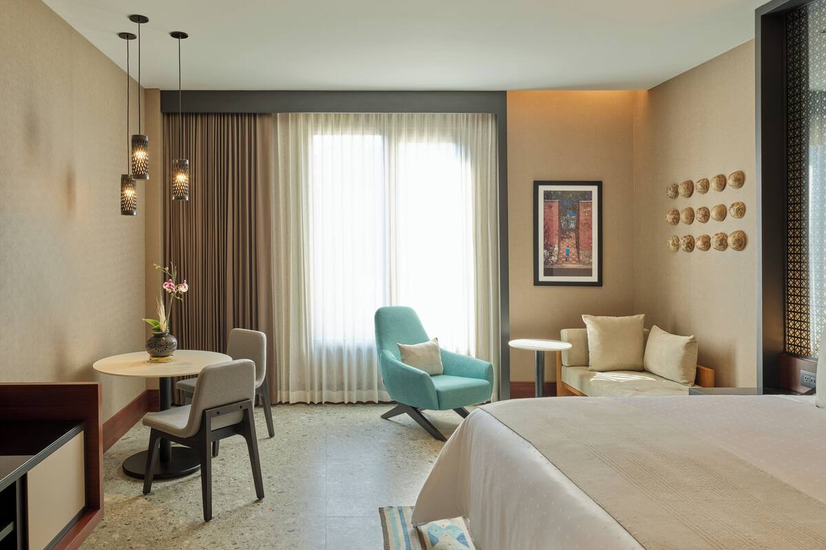 Une chambre d’hôtel comprenant un lit, un bureau avec une chaise, une petite table et un fauteuil de couleur turquoise.