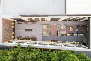 A modern hotel lobby with a central seating area, multiple small tables, and a variety of decorative planters.