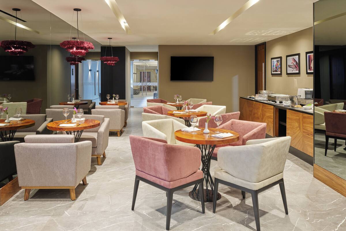 Un restaurant moderne avec des tables rondes, des chaises rembourrées et des luminaires suspendus.