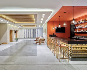 A modern bar area with a long counter, multiple bar stools, and a wall-mounted TV.