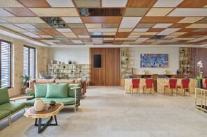 A spacious living area with a wooden ceiling, a green sofa set, a coffee table, and a bar area with red chairs.