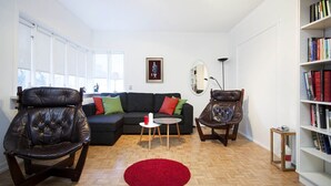 Una sala de estar con un sofá modular, sillones de cuero, una mesita redonda, una alfombra roja, una estanter ía y un cuadro enmarcado en la pared.