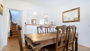 Un comedor con mesa y sillas de madera, un espejo en la pared y una escalera que lleva a otra habitación.