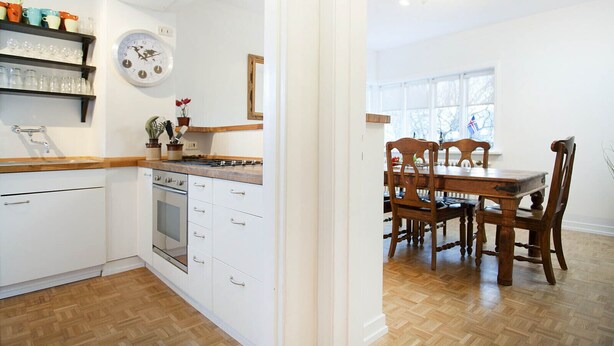 Una cocina con armarios blancos, una estufa y un comedor con sillas de madera y una mesa.