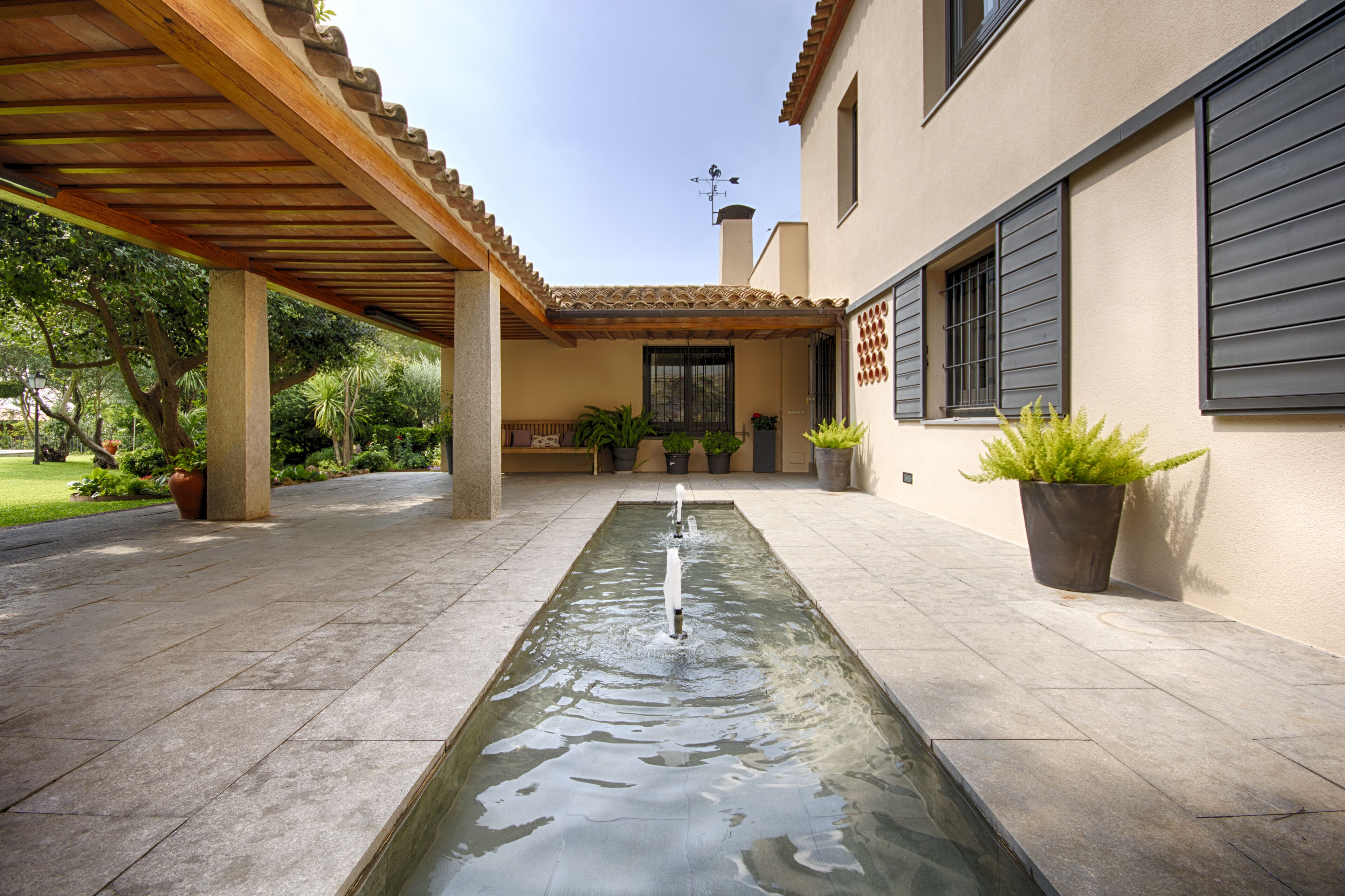 A courtyard with a rectangular water feature, a pergola, and potted plants.