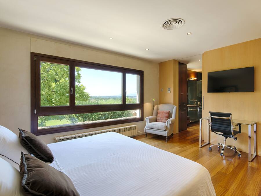 Una habitación de hotel moderna con una cama grande, un escritorio con silla, televisión y vistas al exterior.