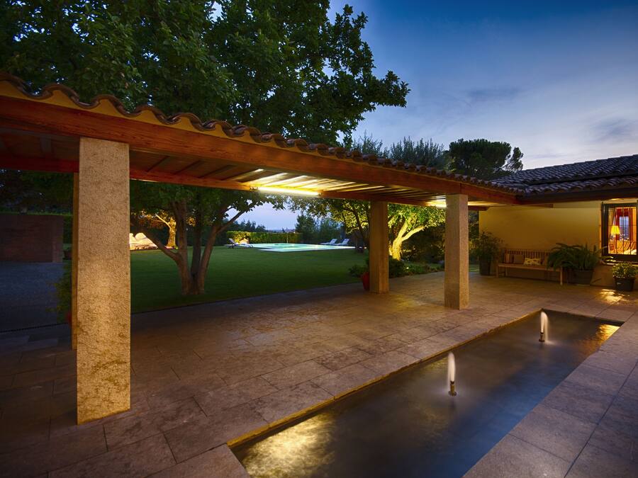 A covered patio with a fountain, a lawn, and a building with a tiled roof.