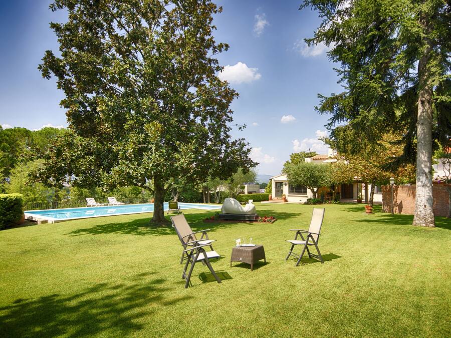 Um gramado bem cuidado com duas cadeiras de descanso e uma mesa pequena, uma piscina e um gazebo ao fundo.