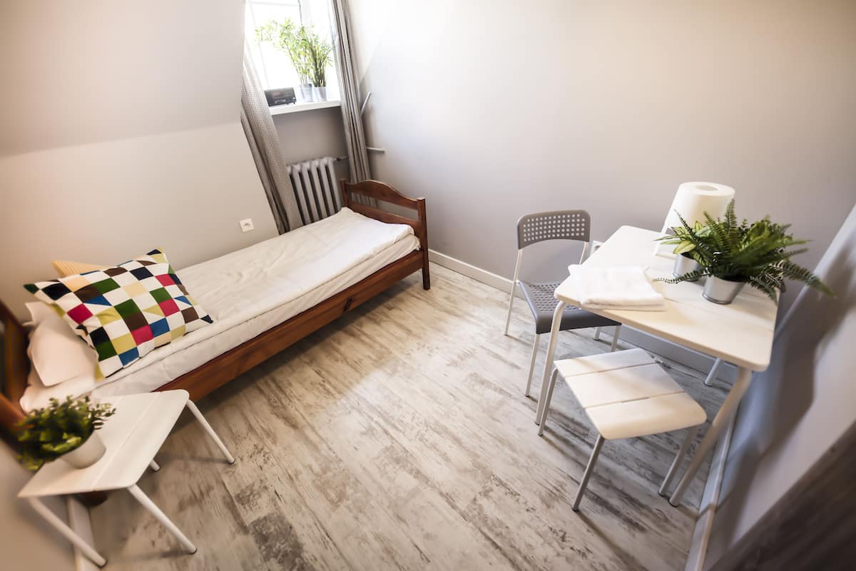 A small, cozy room with a single bed, a chair, a small table, and a radiator.