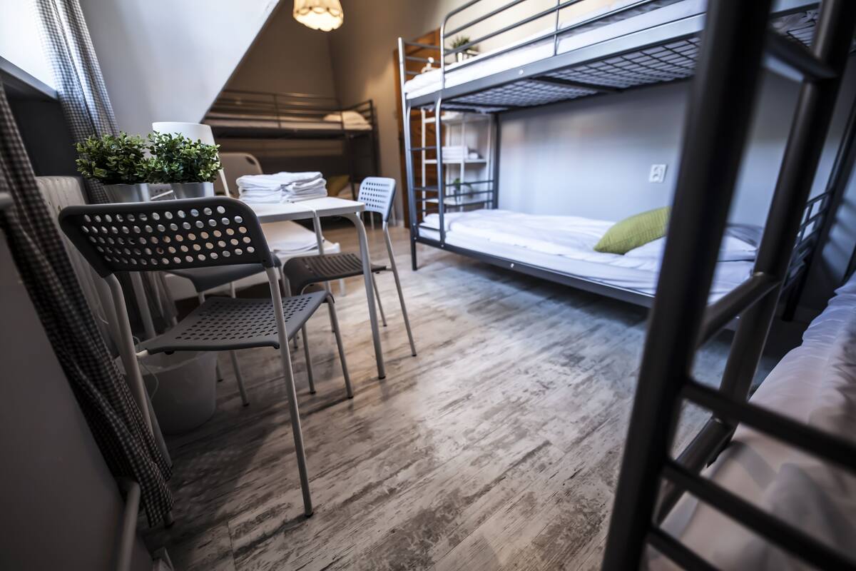 A dormitory room with bunk beds, a desk, chairs, and a small table.