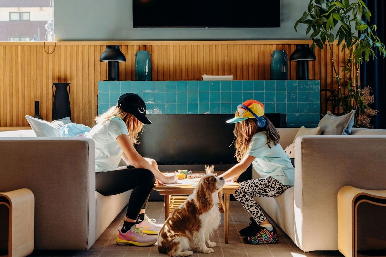 A room with a wooden wall, a flat-screen TV, a table with a dog, and two people sitting on a couch.