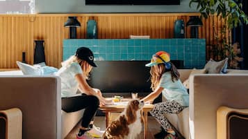 A room with a wooden wall, a flat-screen TV, a table with a dog, and two people sitting on a couch.