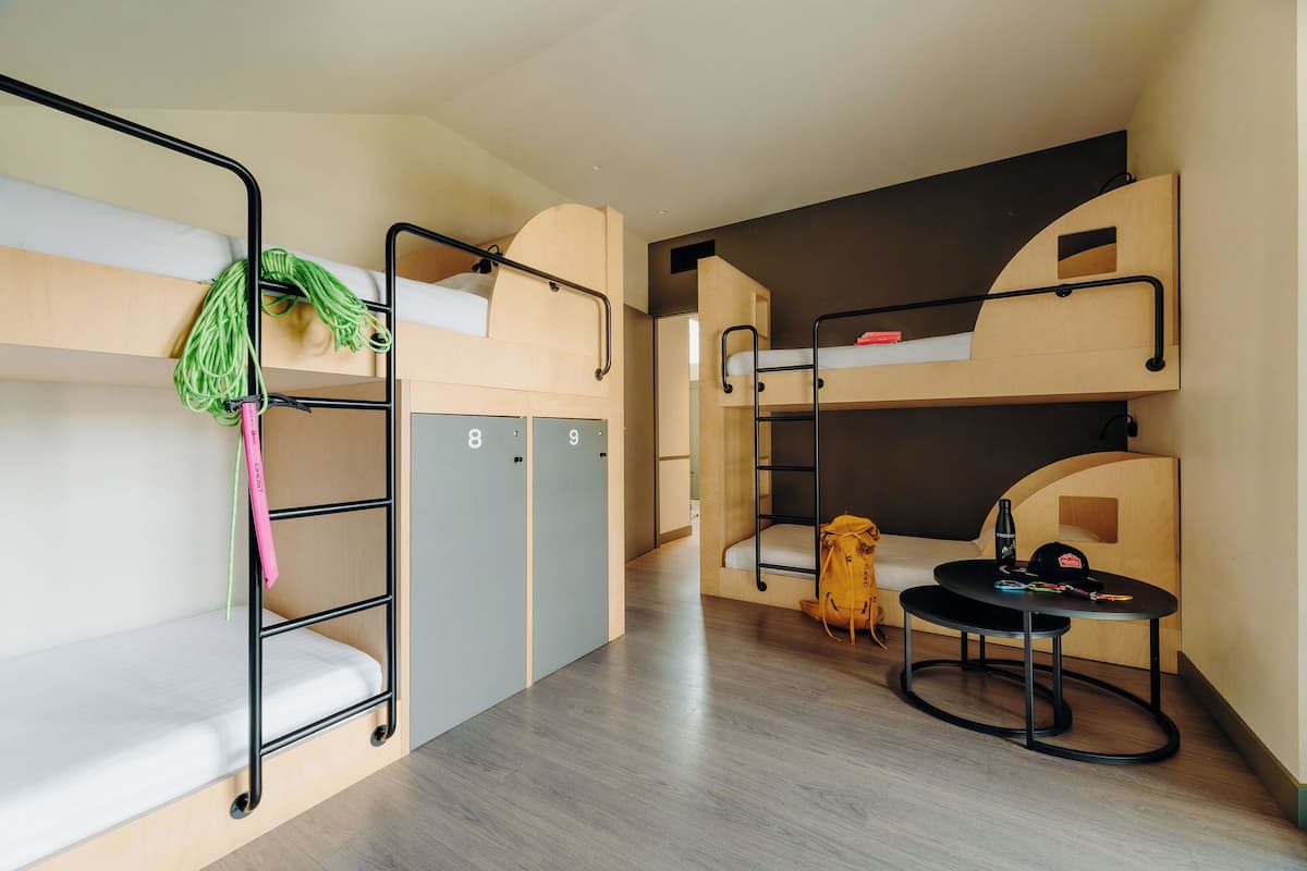A bunk bed room with a desk and chair, a small table, and a backpack.