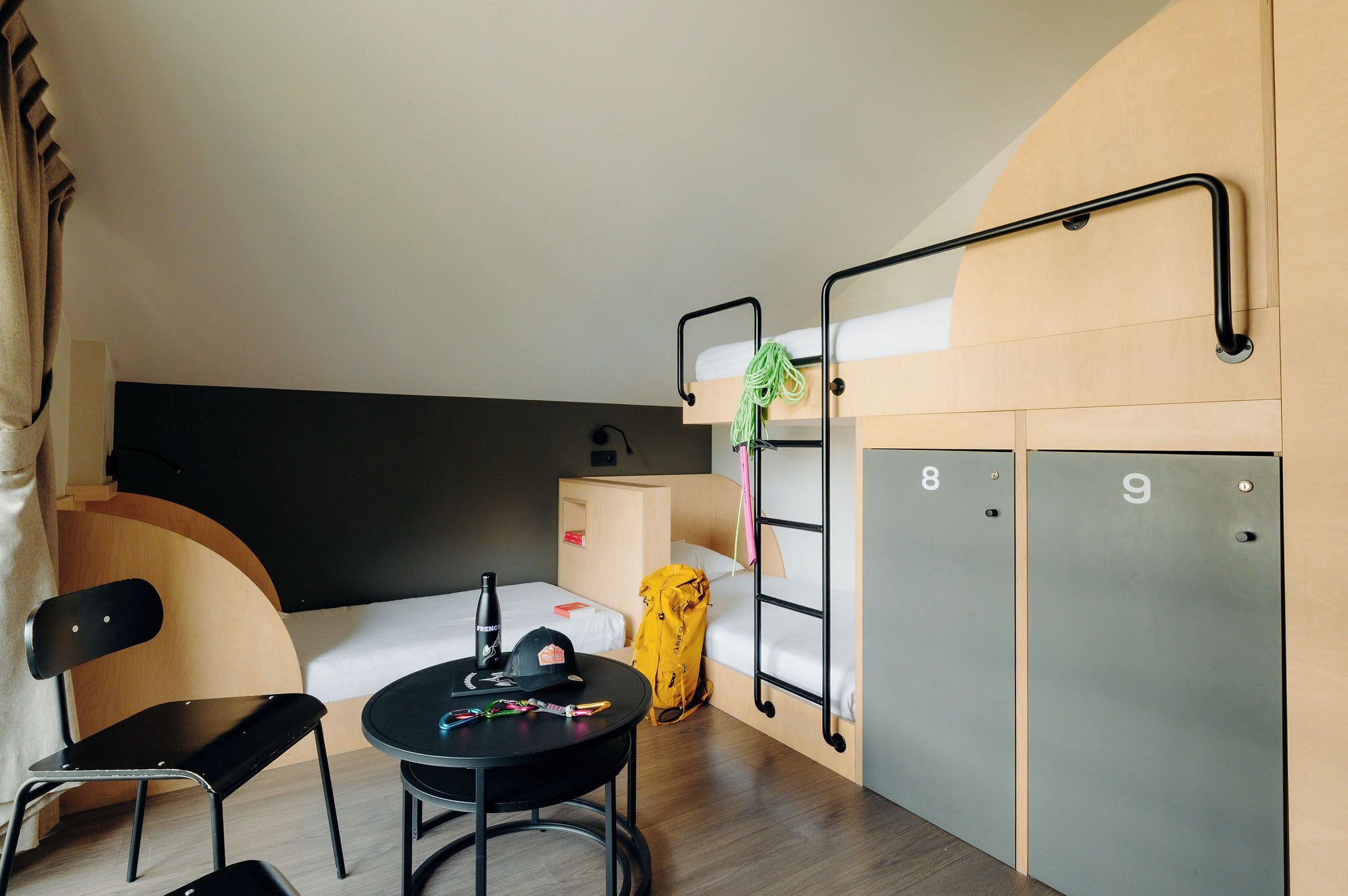 A compact hotel room with bunk beds, a small table with a chair, a desk, and a wardrobe.