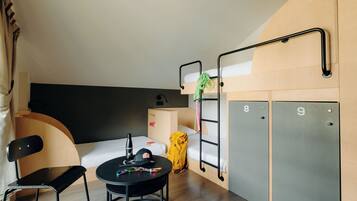 Une chambre d’hôtel compacte avec des lits superposés, une petite table avec une chaise, un bureau et une armoire.