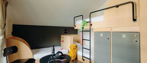 A compact hotel room with bunk beds, a small table with a chair, a desk, and a wardrobe.