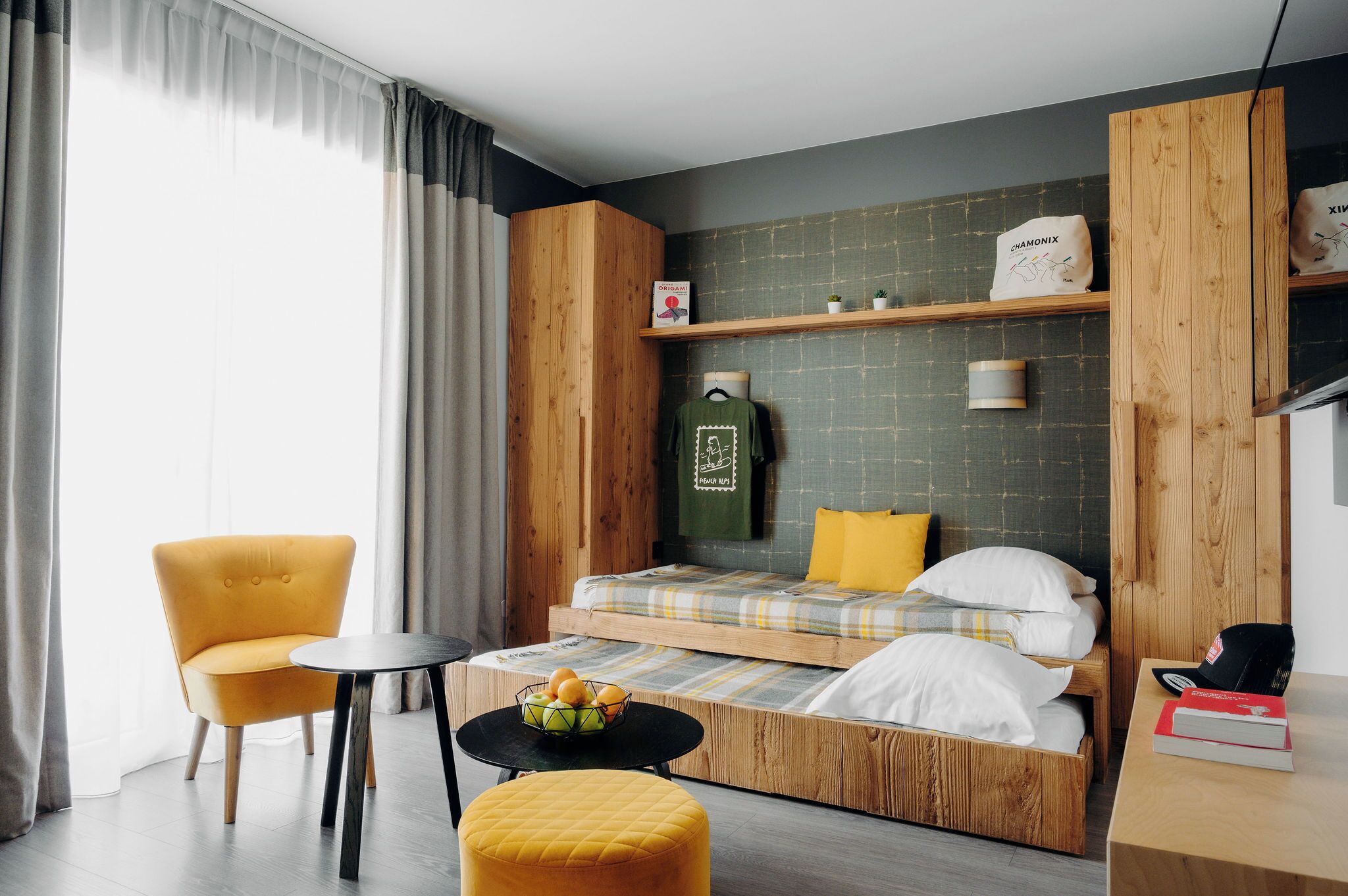 A compact room with a bed, a chair, a small table, and a shelf with items.