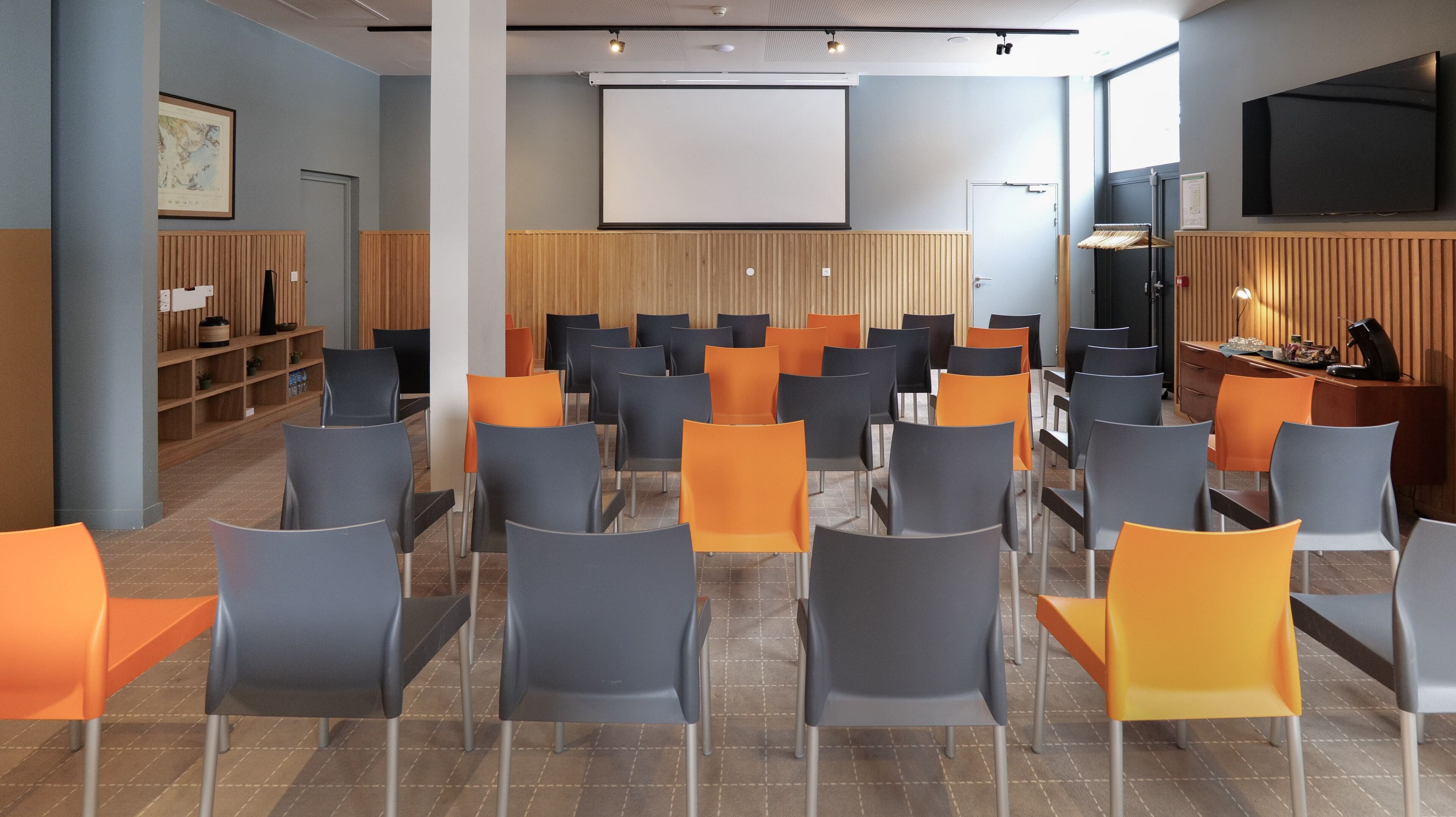 A conference room with rows of chairs, a projector screen, and a television.