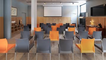 Uma sala de conferência com fileiras de cadeiras, uma tela de projetor e uma televisão.