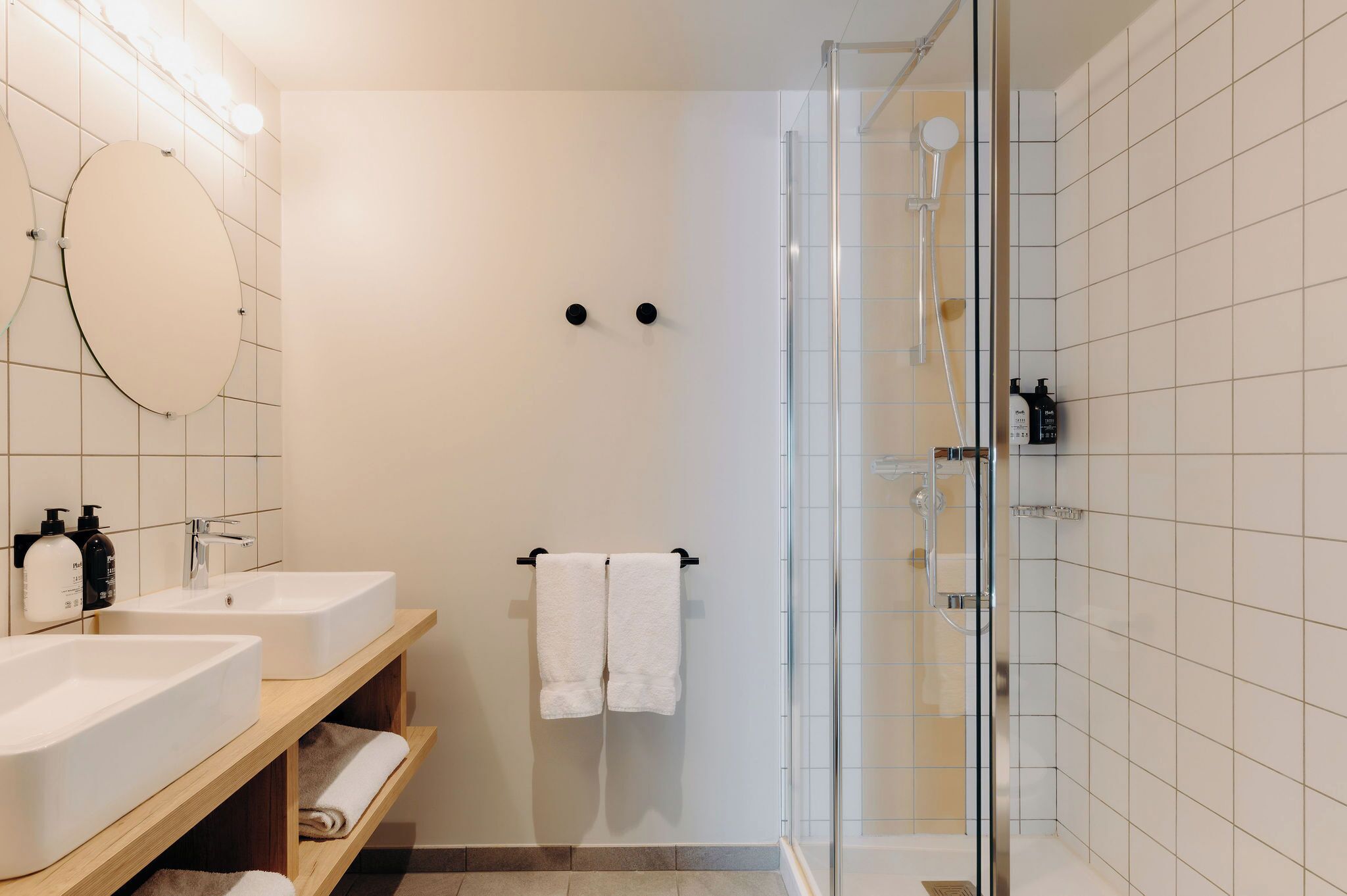 A modern bathroom with two sinks, a glass shower enclosure, and a towel rack.