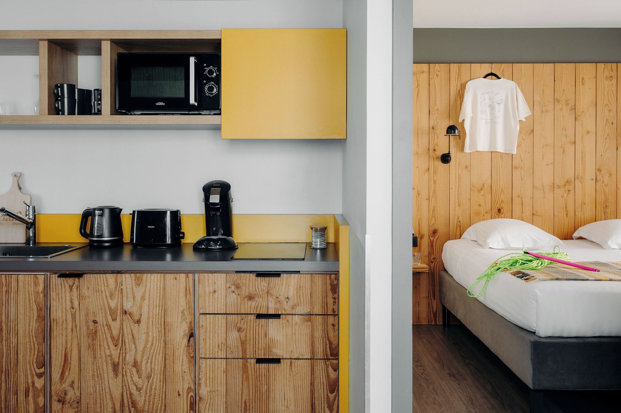 Een kleine kamer met kitchenette, een bed en een houten wand.