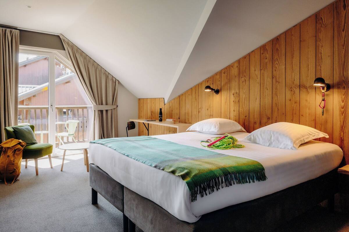 A hotel room with a bed, a desk, a chair, and a balcony with curtains.