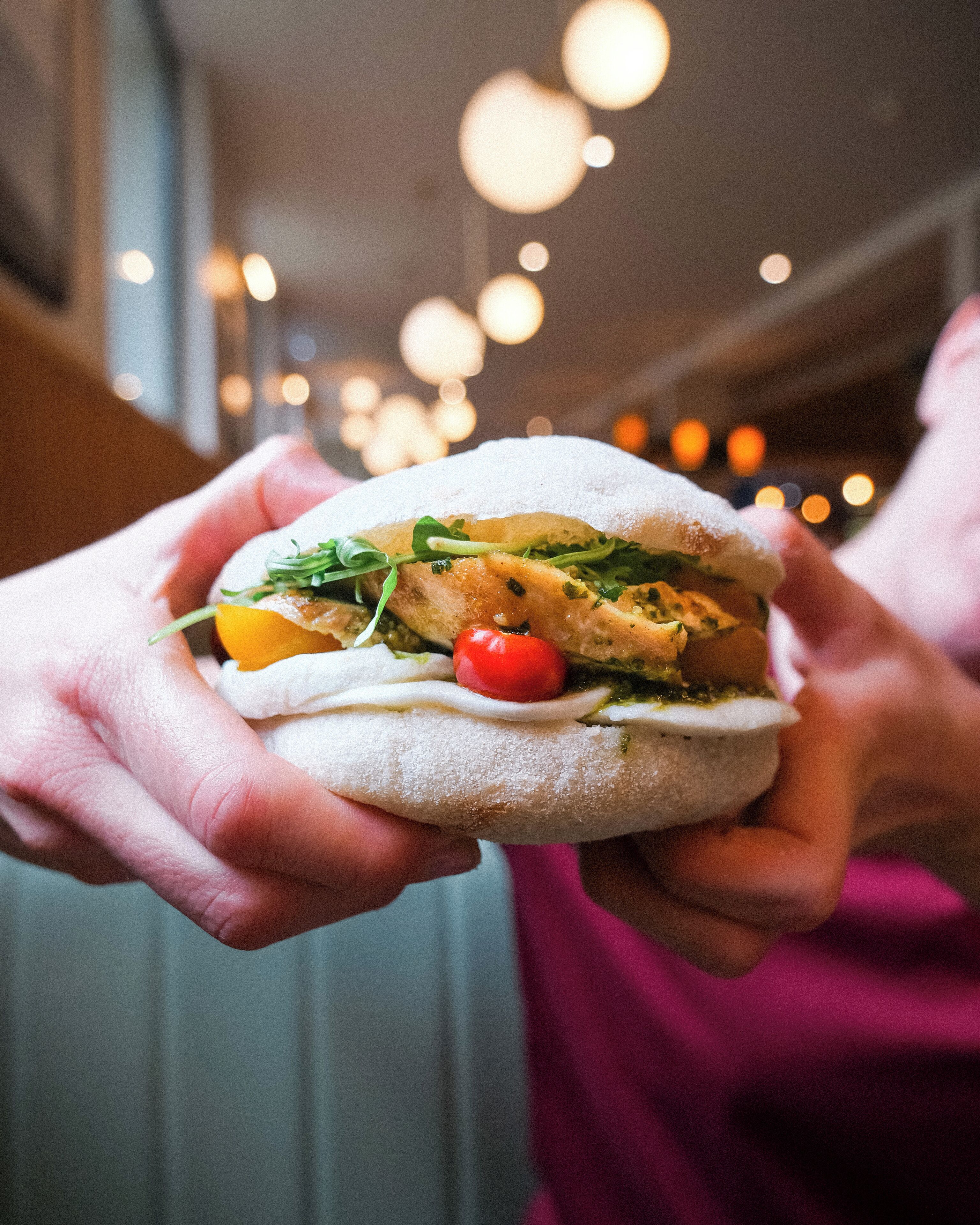 Une personne tenant un sandwich dans lequel on peut voir clairement les ingrédients, comme des légumes verts, des tomates et une tranche de viande.