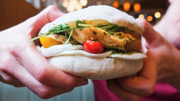 Une personne tenant un sandwich dans lequel on peut voir clairement les ingrédients, comme des légumes verts, des tomates et une tranche de viande.
