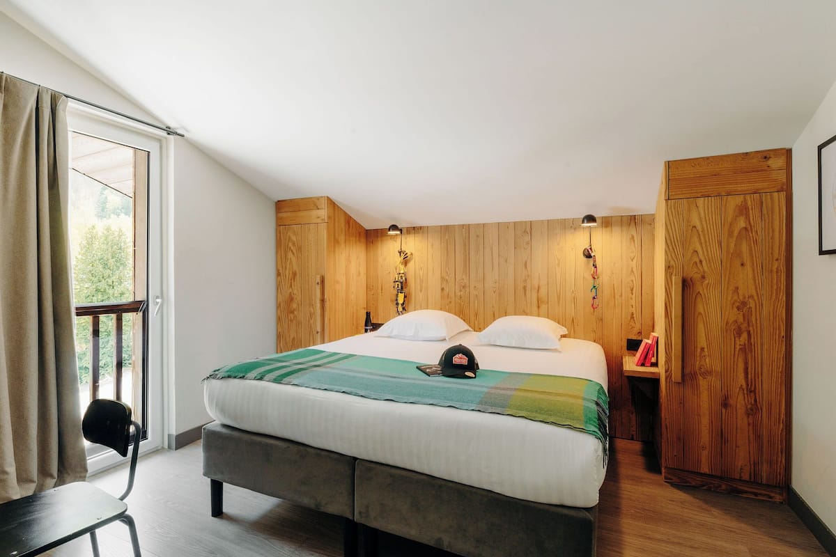 A bedroom with a bed, a chair, a wooden wardrobe, and a window with curtains.