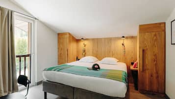 Un dormitorio con cama, una silla, un armario de madera y una ventana con cortinas.