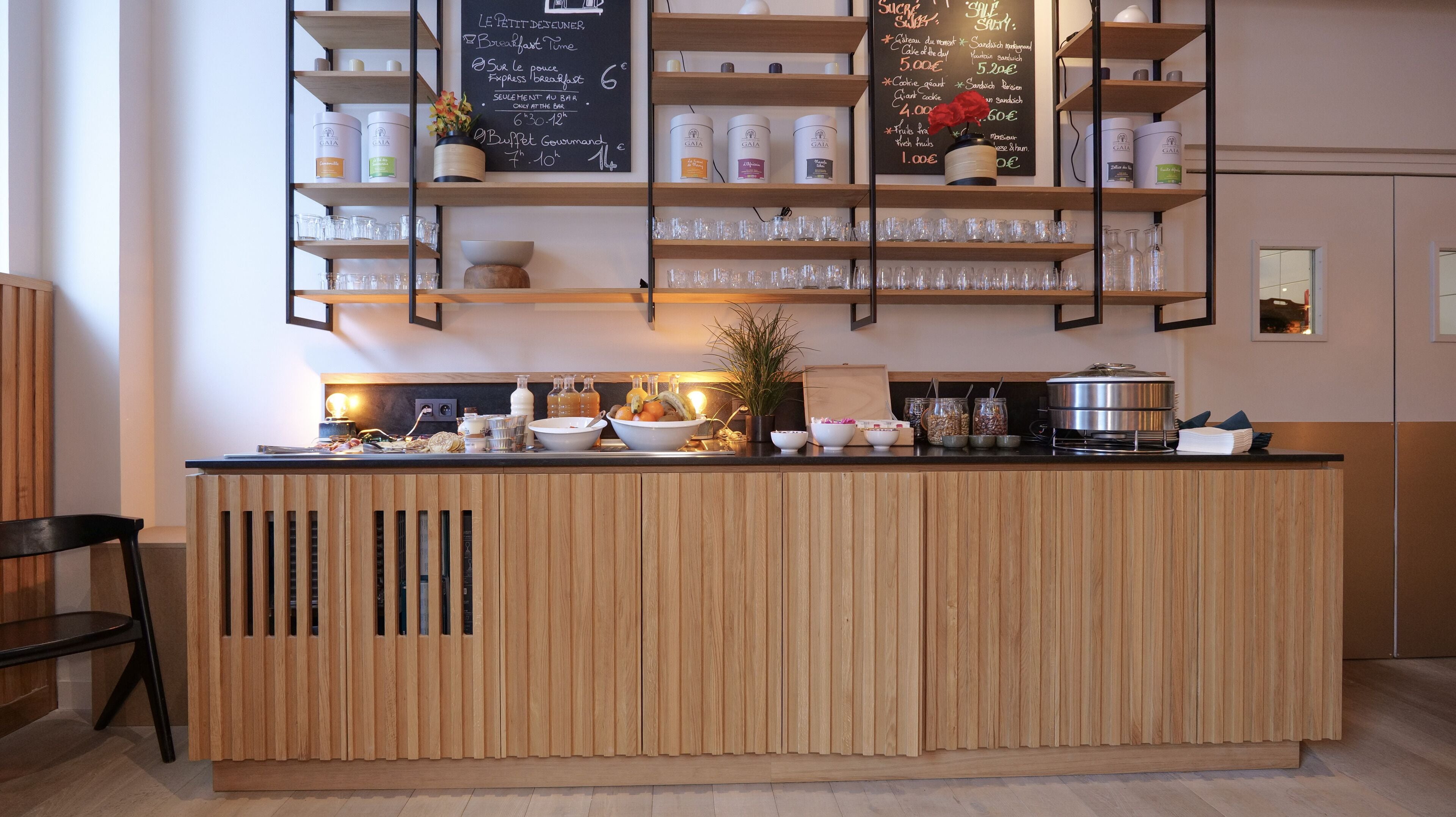 Un bar à petit-déjeuner avec un comptoir en bois, des étagères remplies de bocaux et un tableau noir servant de menu.