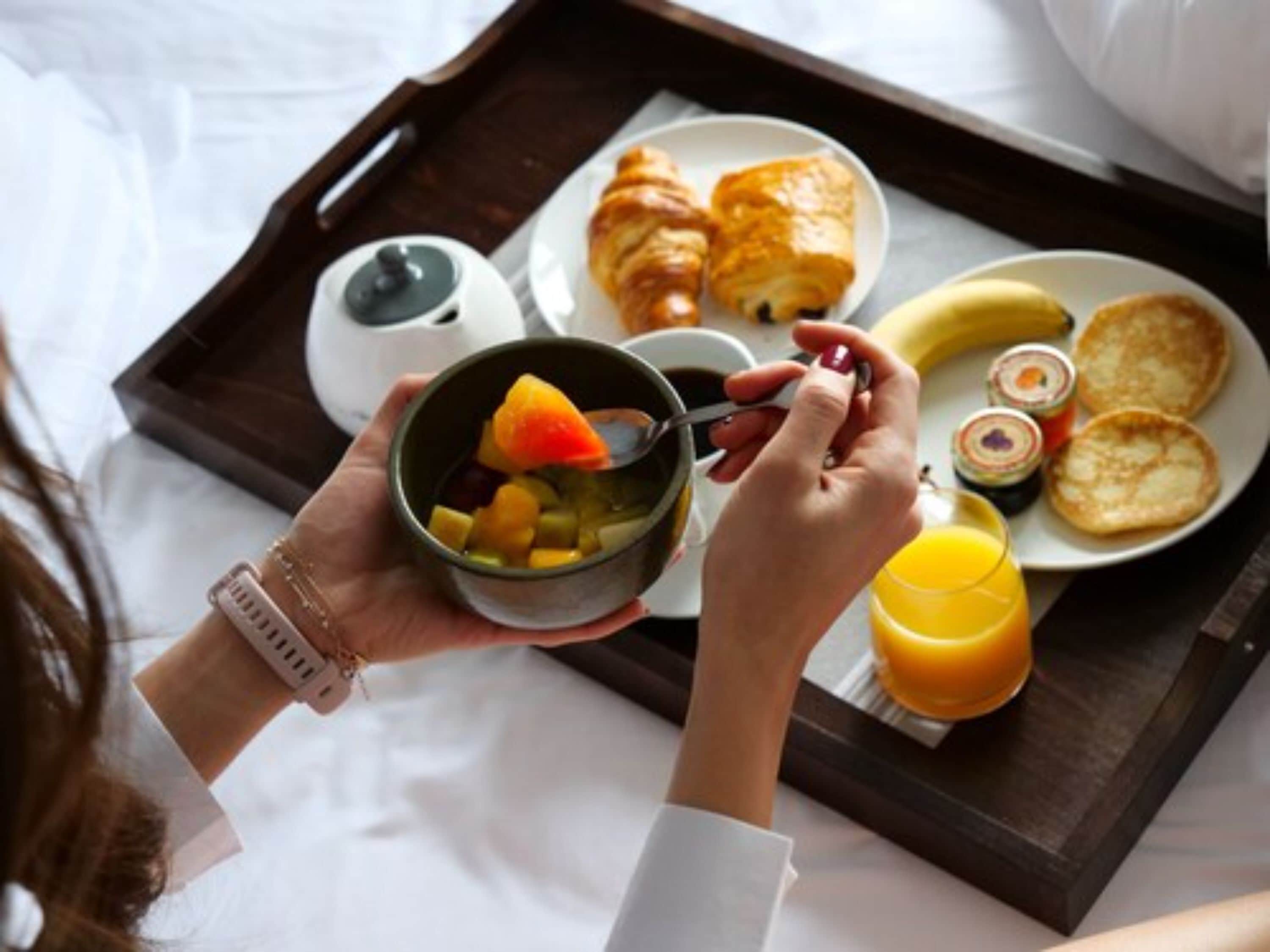 A breakfast tray with croissants, fruit, a cup of coffee, and a glass of orange juice.