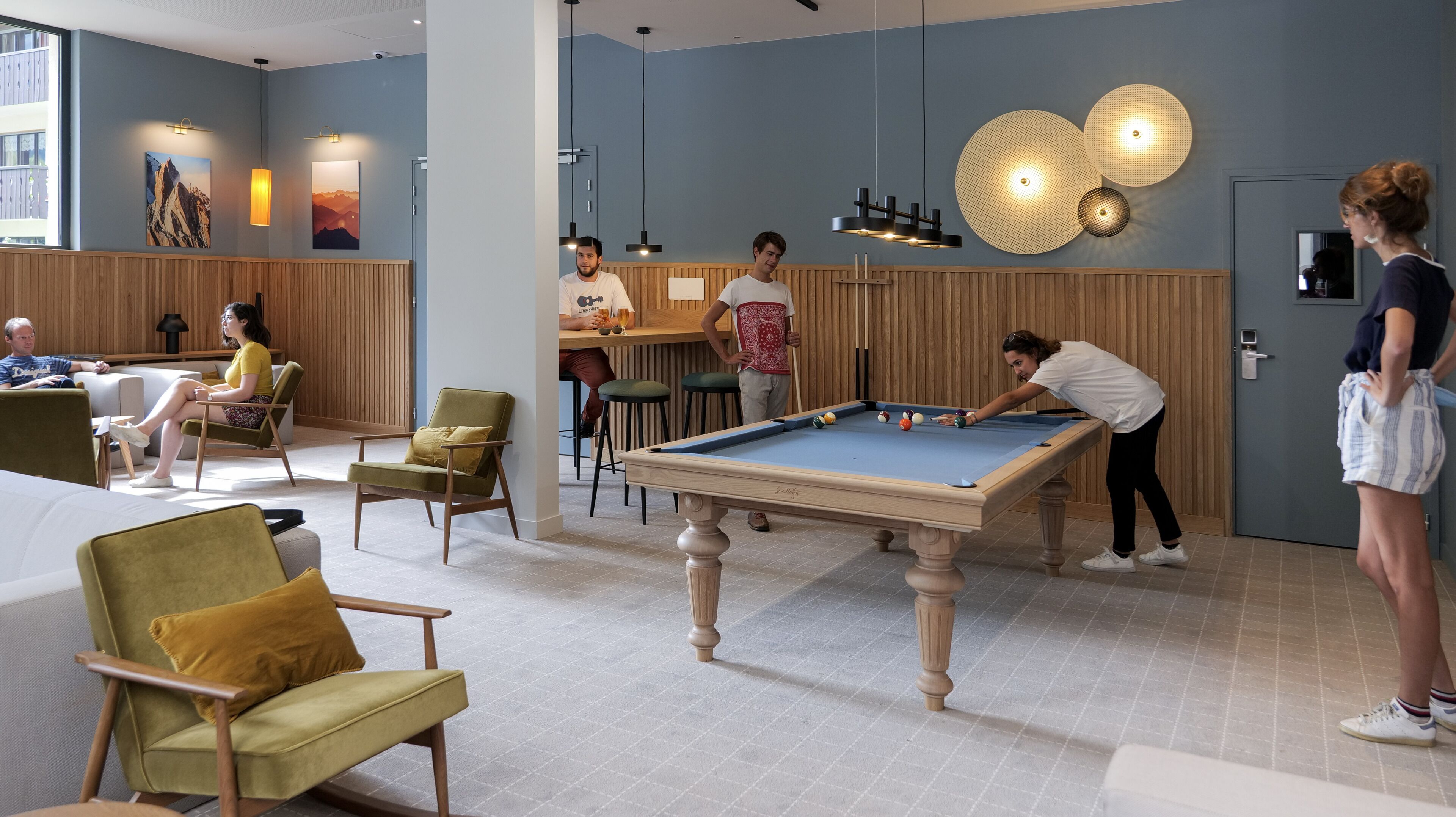 A pool table in a modern lounge area with wooden paneling and comfortable seating.