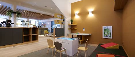 A modern interior with a wooden reception desk, seating area with colorful cushions, and a wall-mounted display.