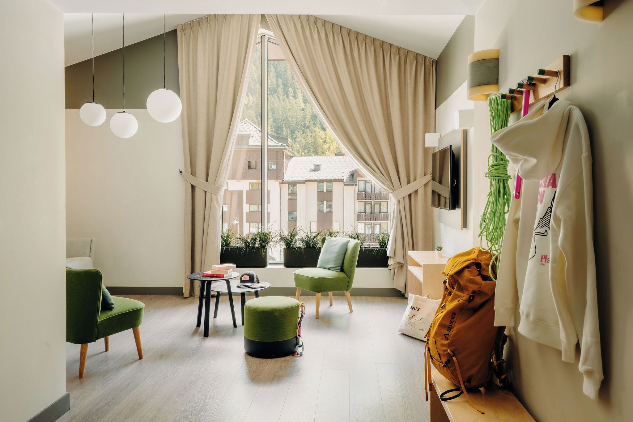 Ein modernes Wohnzimmer mit großem Fenster, einem grünen Sessel, einem runden Hocker und einem wandmontierten Fernseher.