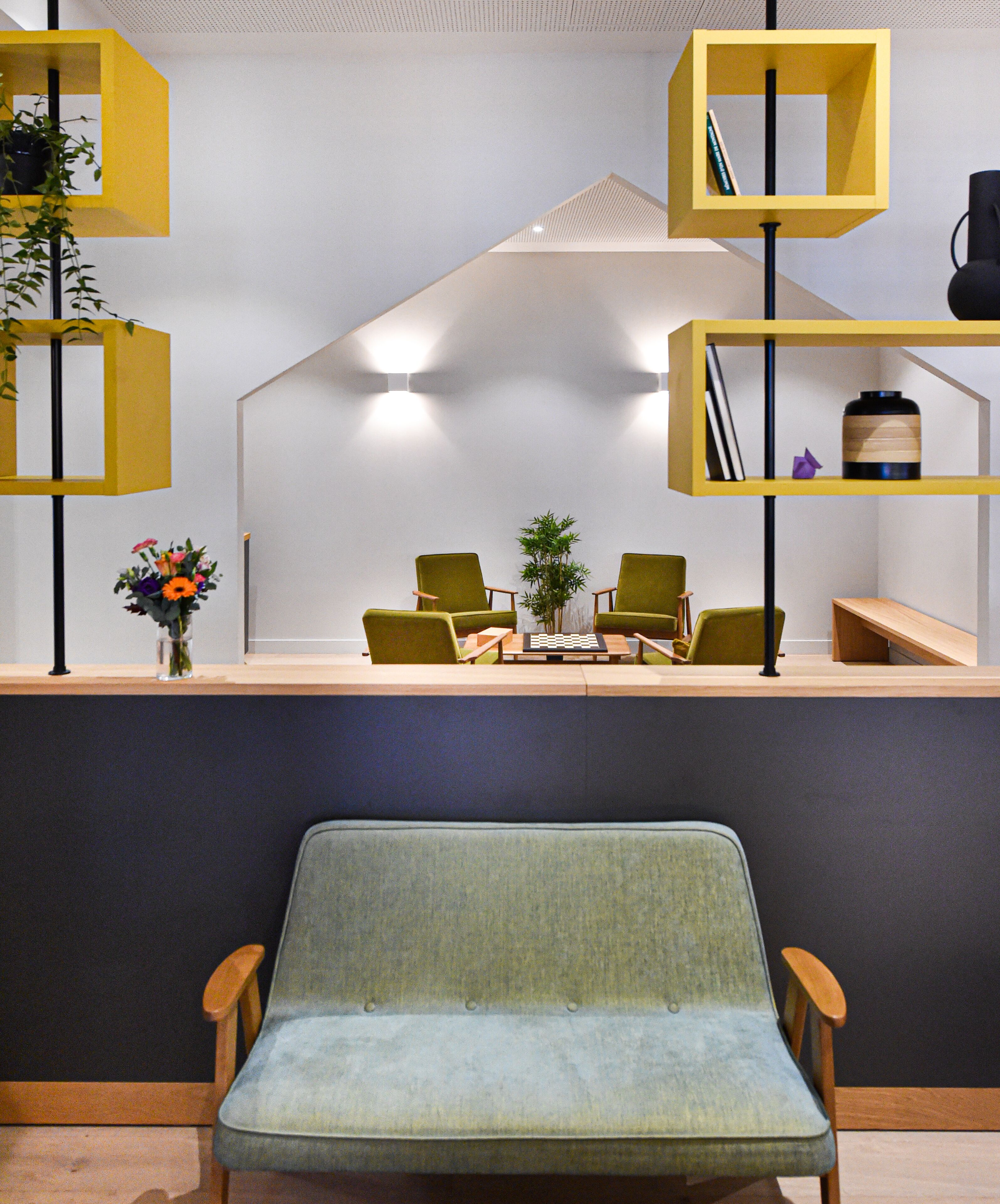 A modern interior with a green upholstered chair, a chess table, and yellow shelving units.