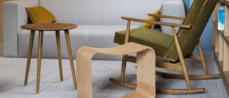 A modern living room with a grey sofa, a wooden rocking chair, and a small wooden table.