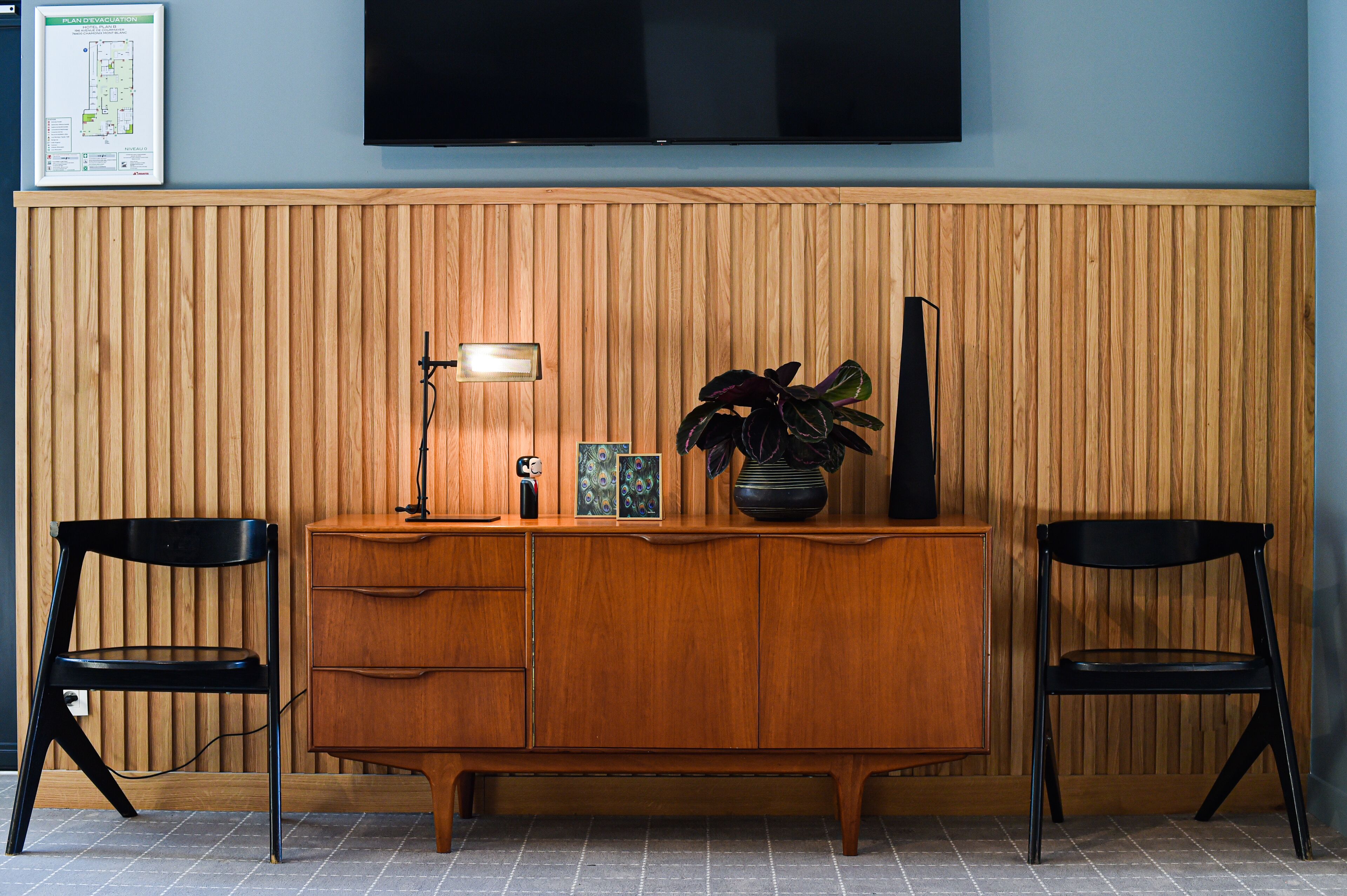 Een houten receptiebalie met een flatscreen televisie erboven, twee zwarte stoelen en een potplant.