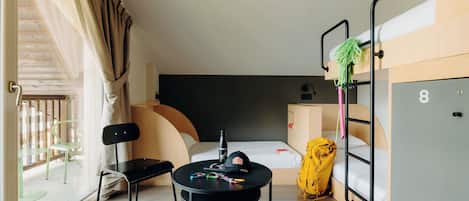 A hotel room with a bed, a desk, a chair, a table, a bunk bed, and a window with curtains.