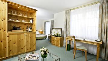 Ein Zimmer mit einem Holzkasten, einem Glastisch mit einer Vase, einem Bett, einem Schreibtisch und einem Stuhl.