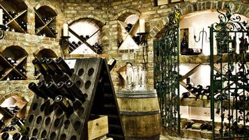 A wine cellar with wooden racks, barrels, and a stone wall with arched niches.