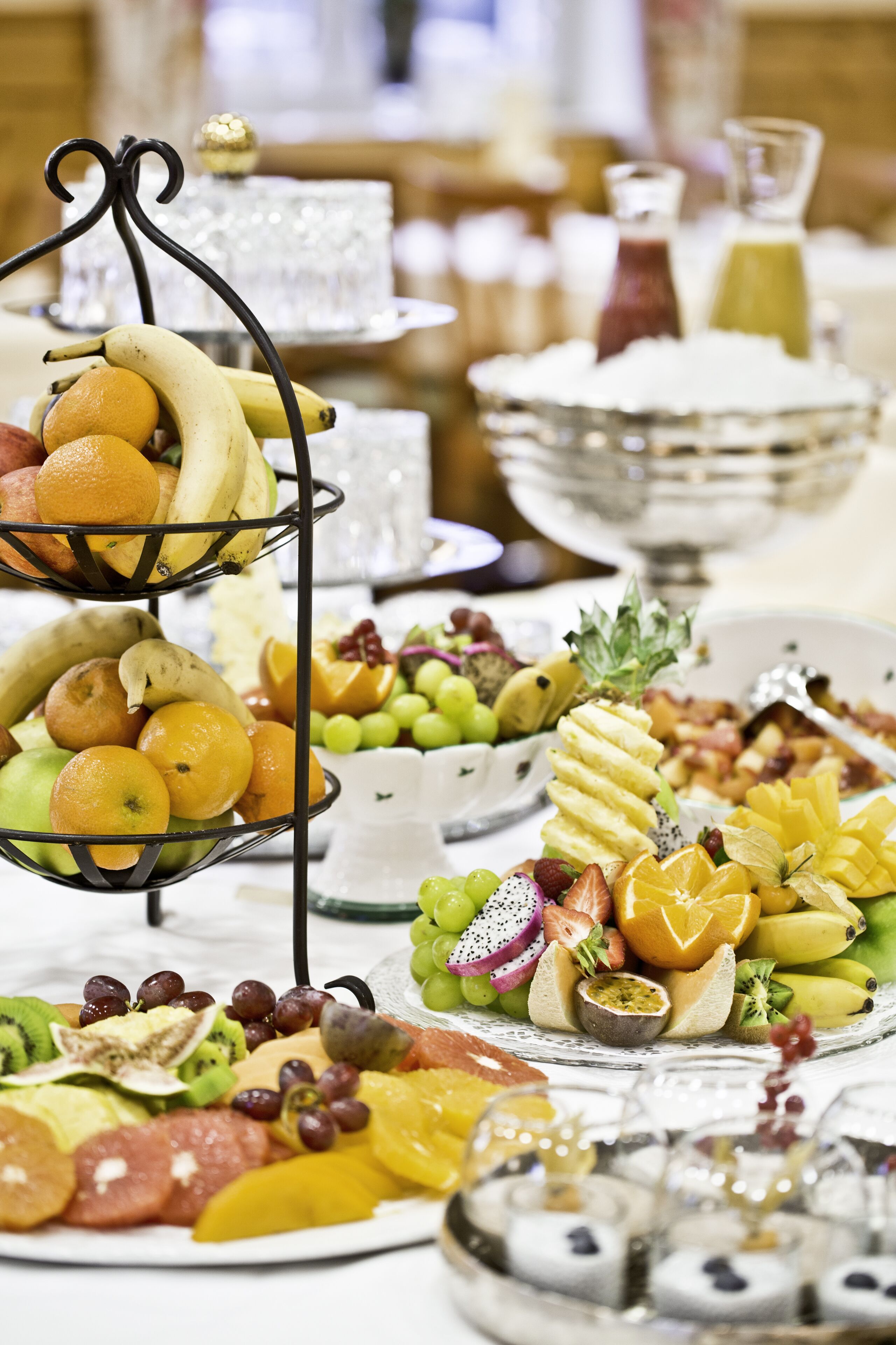 A buffet table with various fruits, cheeses, and a decorative metal stand.