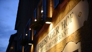 Een bord met daarop 'FREISINGER HOTEL-RESTAURANT' met verlichte letters en bloembakken.