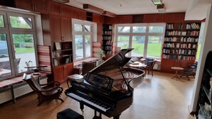 A spacious living room with a grand piano, a bookshelf, and a window with a view of the outdoors. - Sund (Grosefehn)