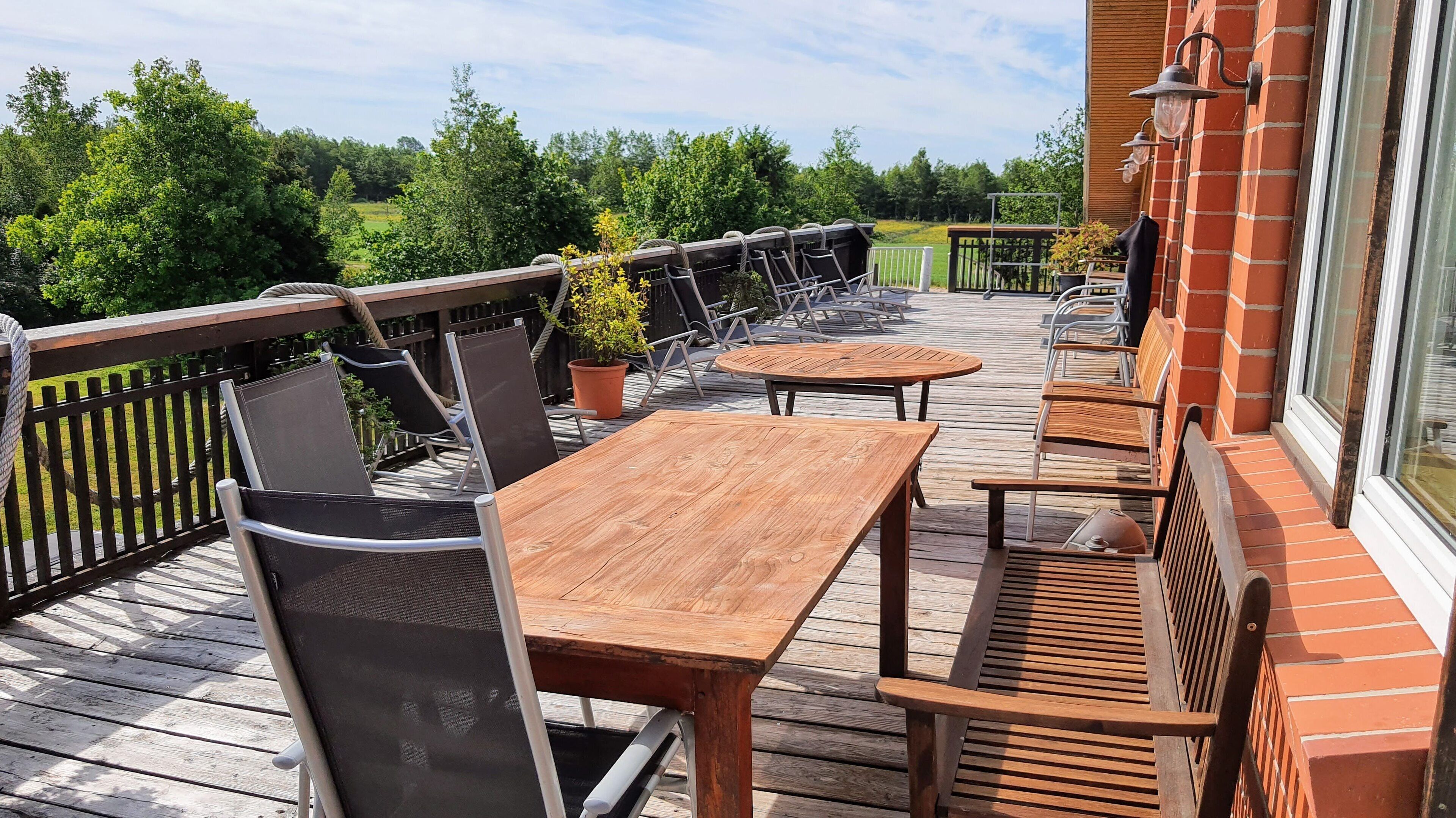 A wooden deck with outdoor seating, including tables and chairs, overlooking a green landscape.