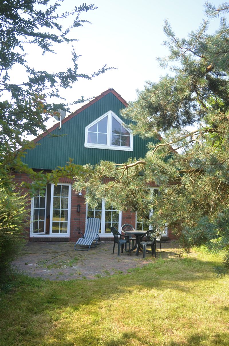 Une maison avec un toit végétalisé, une façade en briques et une terrasse aménagée avec du mobilier d’extérieur.