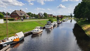 A canal with boats docked on the left side, surrounded by houses and greenery. - Sund (Grosefehn)