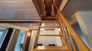A wooden staircase leading to an upper floor, with a chandelier and a plant visible. - Sund (Grosefehn)