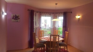 Un comedor con mesa y sillas, una ventana con cortinas y vistas a follaje exterior.